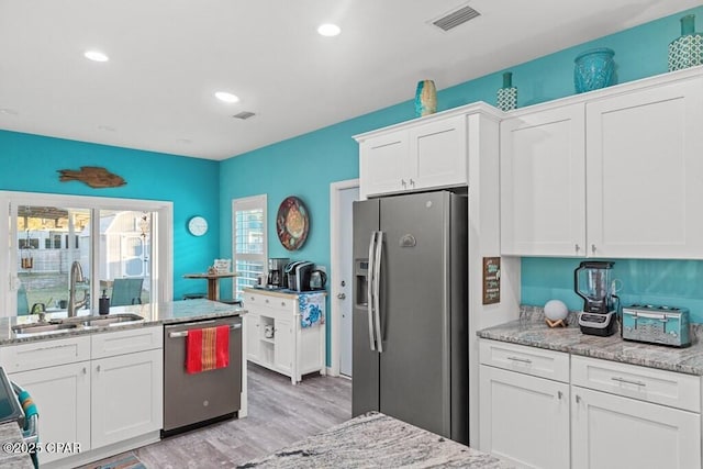 132 Gulf Terrace Ln, Port St Joe, FL 32456 - kitchen with appliances with stainless steel finishes, a sink, white cabinets, light wood-type flooring, and light stone countertops
