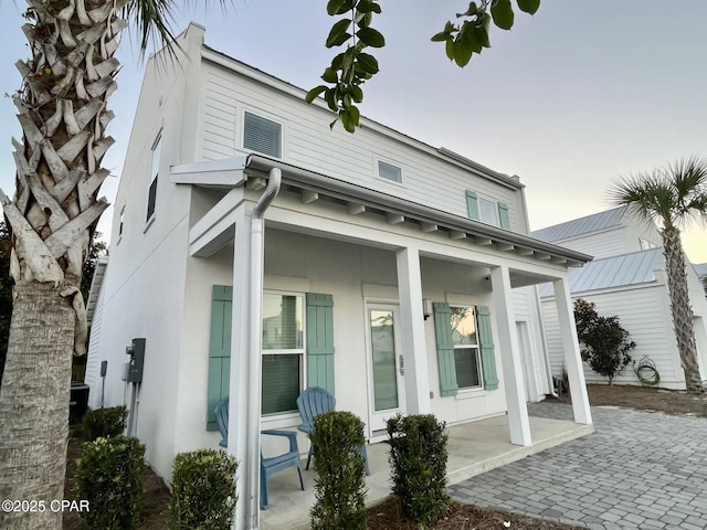 rear view of house with covered porch and stucco siding