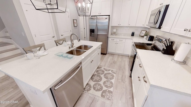 kitchen featuring a center island with sink, stainless steel appliances, light countertops, hanging light fixtures, and a sink