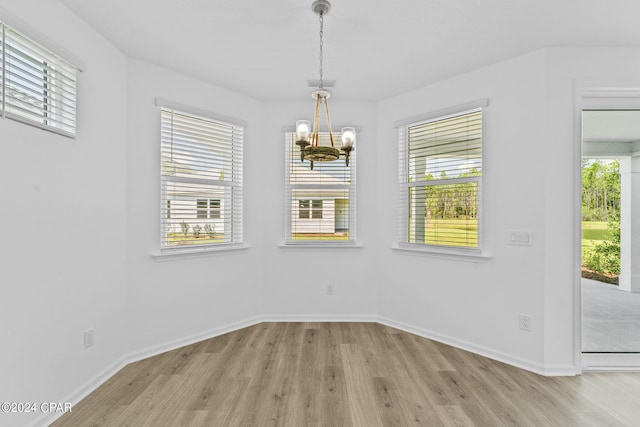 unfurnished dining area featuring a chandelier, light wood-style floors, baseboards, and a wealth of natural light