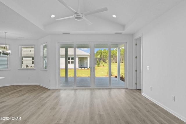 unfurnished living room featuring plenty of natural light, lofted ceiling, wood finished floors, and ceiling fan with notable chandelier