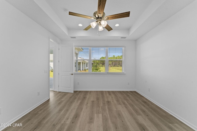 spare room featuring ceiling fan, recessed lighting, wood finished floors, a raised ceiling, and baseboards