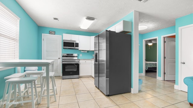 kitchen featuring stainless steel appliances, a textured ceiling, ceiling fan, light tile patterned floors, and white cabinetry