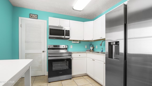 kitchen with sink, appliances with stainless steel finishes, white cabinets, and light tile patterned floors