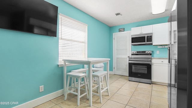 kitchen featuring light tile patterned flooring, appliances with stainless steel finishes, and white cabinetry