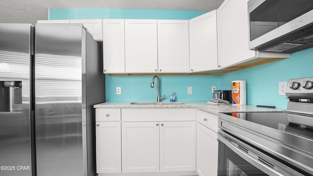 kitchen featuring appliances with stainless steel finishes, sink, white cabinetry, and light stone countertops