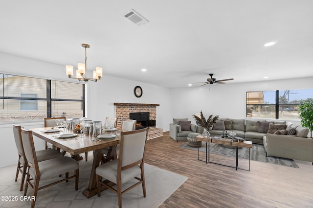 dining room featuring a brick fireplace, hardwood / wood-style flooring, and ceiling fan with notable chandelier