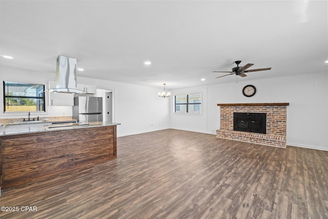 unfurnished living room with dark hardwood / wood-style flooring, sink, a brick fireplace, and ceiling fan with notable chandelier