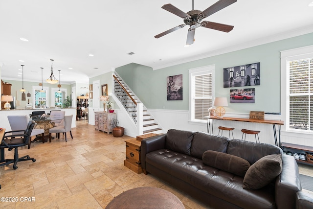 living room with stairs, stone tile flooring, crown molding, and a ceiling fan