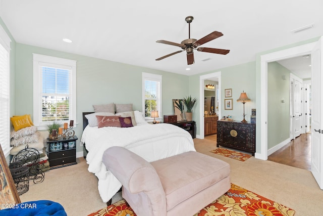 bedroom with ensuite bath, visible vents, ceiling fan, and light colored carpet