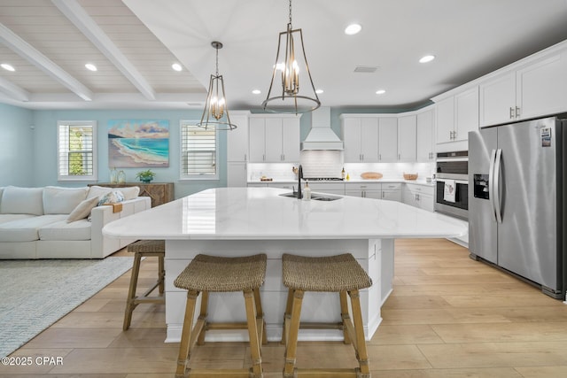 kitchen with white cabinetry, a center island with sink, stainless steel appliances, decorative light fixtures, and custom range hood