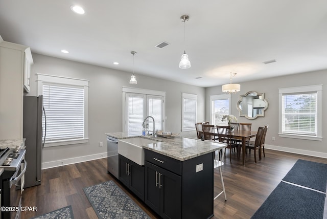 kitchen featuring sink, white cabinets, hanging light fixtures, stainless steel appliances, and a center island with sink