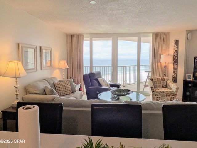 living area with a textured ceiling, a wall of windows, and a water view