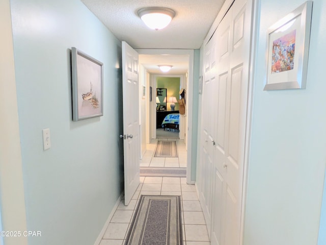 hall with light tile patterned flooring, a textured ceiling, and baseboards