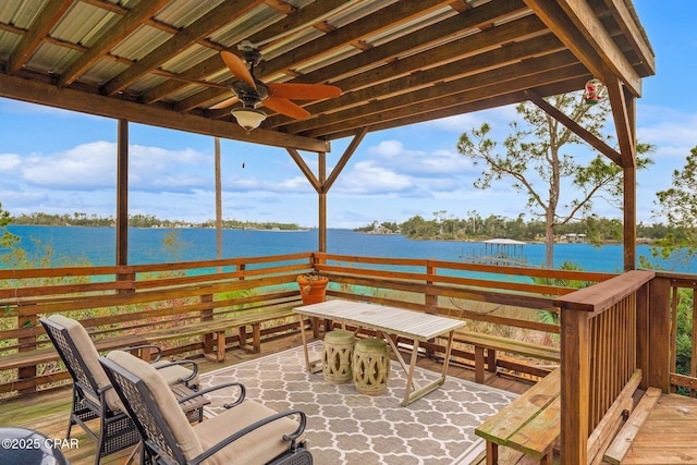 wooden terrace featuring a ceiling fan, outdoor dining space, and a water view