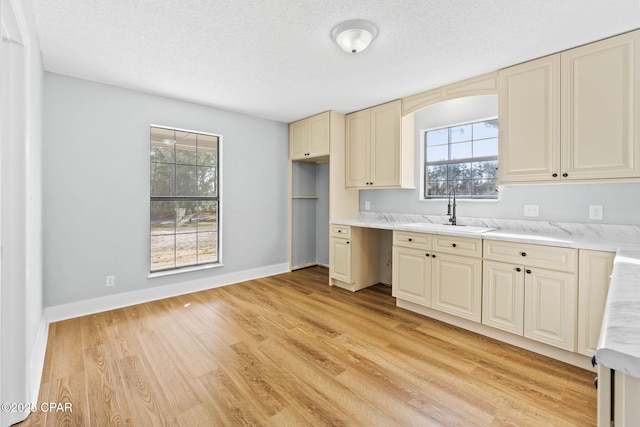 kitchen with cream cabinets, sink, a textured ceiling, and light hardwood / wood-style flooring