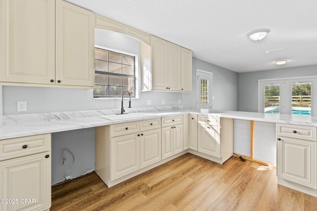 kitchen with sink, kitchen peninsula, cream cabinetry, and light hardwood / wood-style flooring