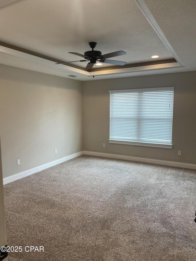 empty room with ceiling fan, a raised ceiling, and carpet floors