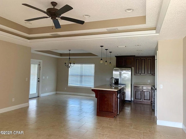 kitchen with a raised ceiling, stainless steel refrigerator with ice dispenser, a center island with sink, and decorative light fixtures