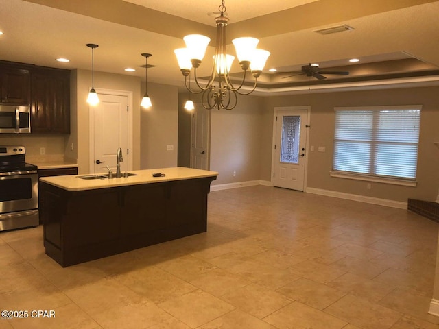 kitchen featuring decorative light fixtures, a raised ceiling, an island with sink, sink, and stainless steel appliances