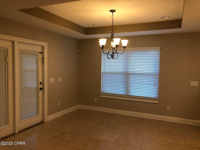 spare room with a tray ceiling and a notable chandelier