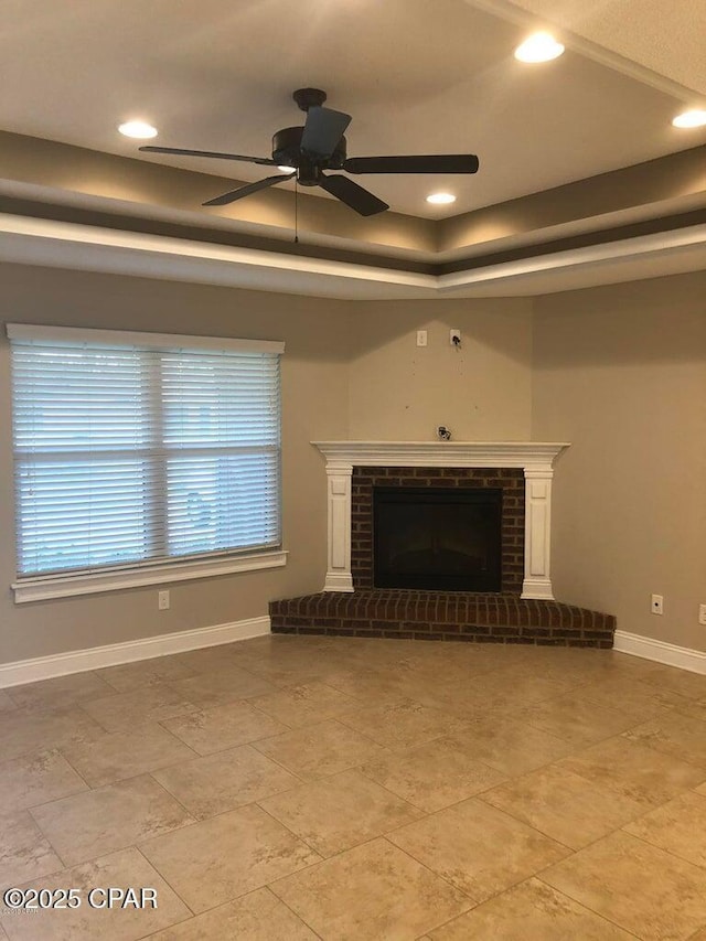 unfurnished living room featuring a brick fireplace, a raised ceiling, and ceiling fan