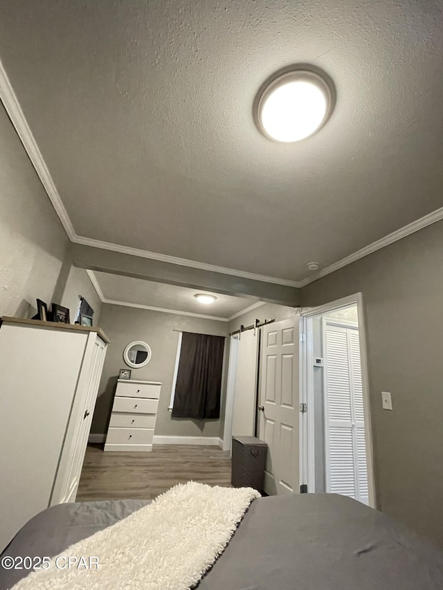 unfurnished bedroom featuring wood-type flooring, ornamental molding, and a barn door