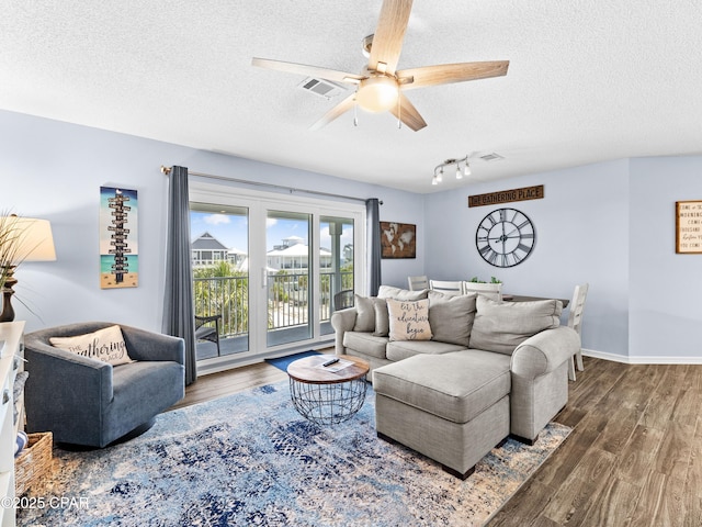 living area with a textured ceiling, ceiling fan, wood finished floors, and visible vents