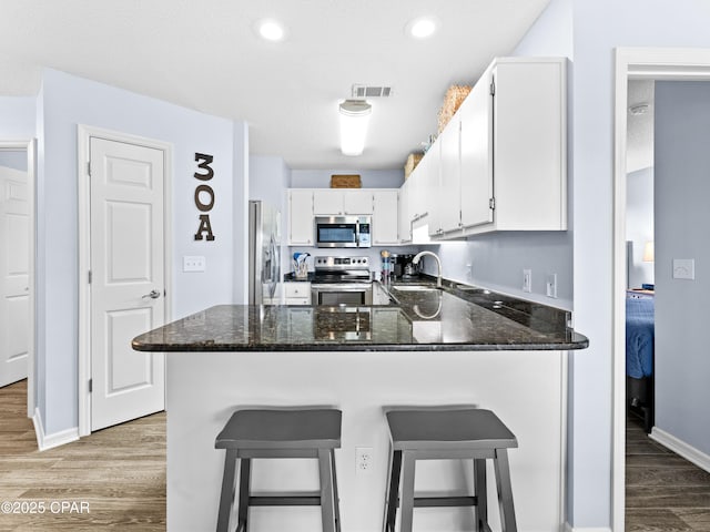 kitchen with light wood finished floors, stainless steel appliances, visible vents, white cabinets, and a sink