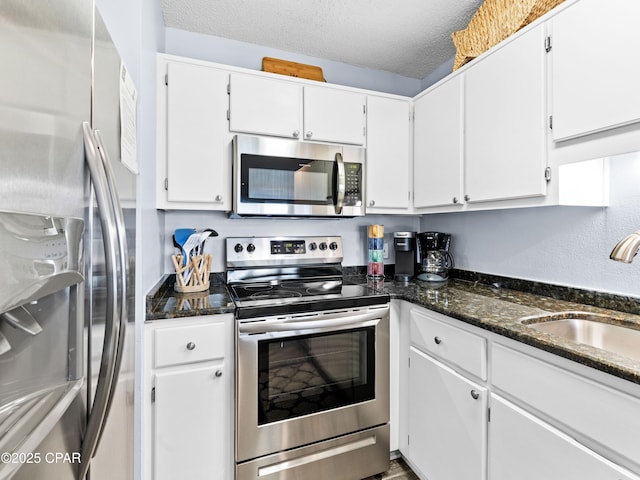 kitchen featuring white cabinets, dark stone countertops, stainless steel appliances, a textured ceiling, and a sink