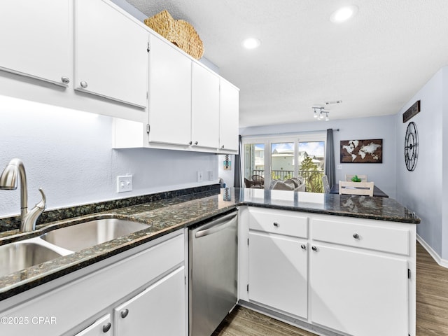 kitchen with wood finished floors, a peninsula, stainless steel dishwasher, and a sink