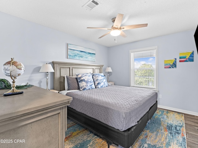 bedroom with dark wood-style floors, visible vents, a ceiling fan, a textured ceiling, and baseboards