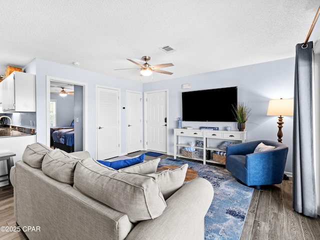 living area featuring visible vents, ceiling fan, a textured ceiling, and wood finished floors