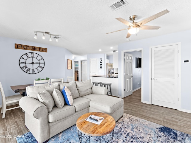 living area featuring baseboards, a textured ceiling, visible vents, and wood finished floors