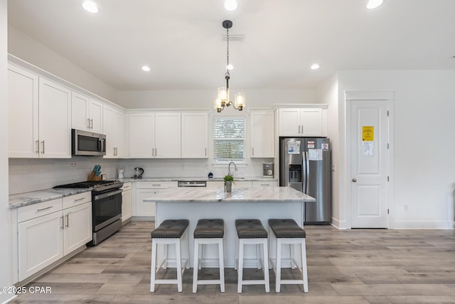 kitchen with stainless steel appliances, white cabinetry, a center island, and light stone counters