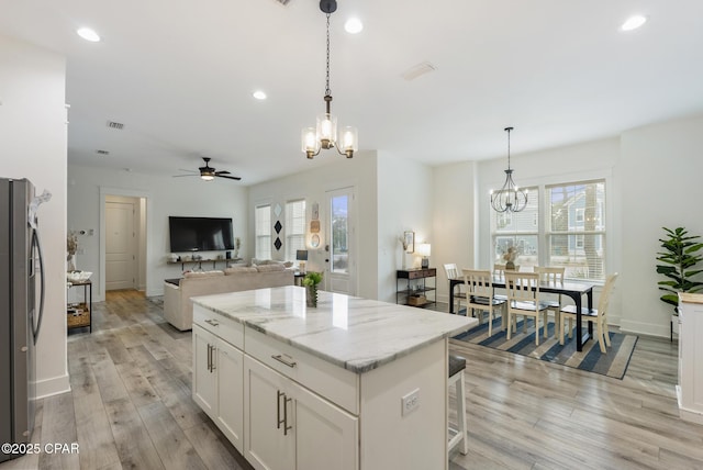 kitchen with white cabinets, light stone countertops, stainless steel fridge, and decorative light fixtures