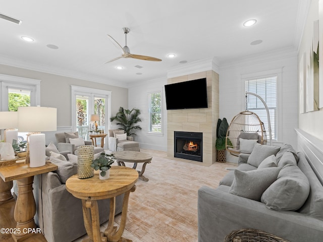 living area featuring ceiling fan, a tiled fireplace, recessed lighting, visible vents, and ornamental molding