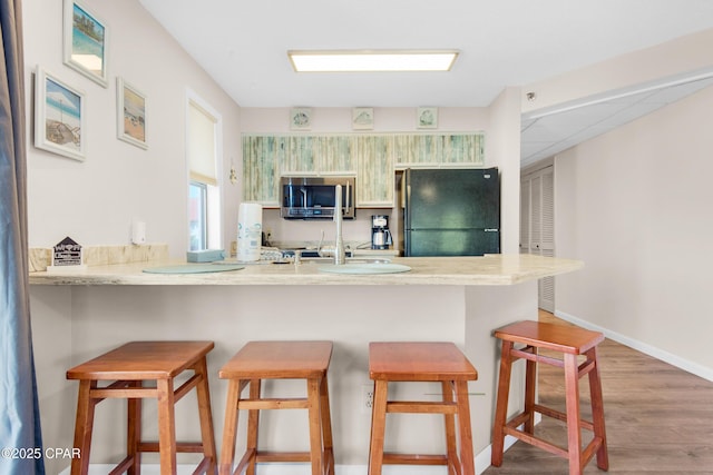 8730 Thomas Dr Unit 1211C, Panama City Beach, FL 32408 - kitchen with a kitchen breakfast bar, stainless steel microwave, freestanding refrigerator, wood finished floors, and a peninsula