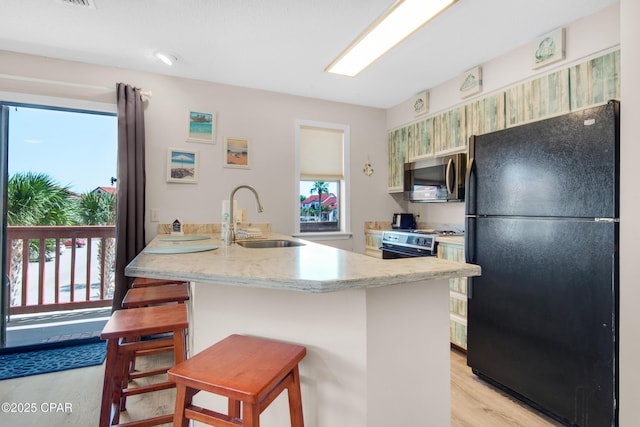 kitchen with light wood finished floors, appliances with stainless steel finishes, a sink, a peninsula, and a kitchen bar