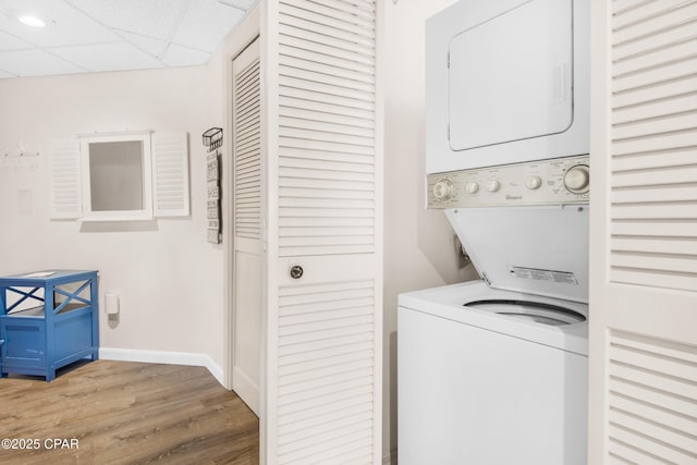 laundry room featuring laundry area, stacked washer / dryer, light wood-type flooring, and baseboards