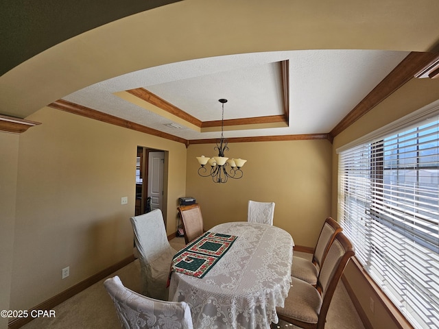 dining space featuring crown molding, a tray ceiling, carpet flooring, and a notable chandelier