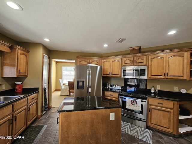 kitchen with dark stone counters, stainless steel appliances, a textured ceiling, and a center island