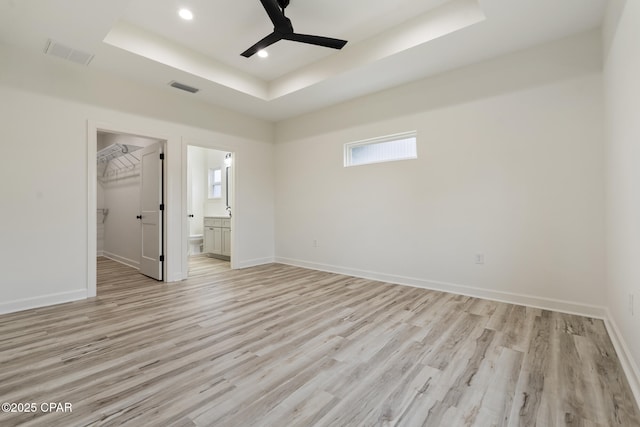 unfurnished bedroom with light wood-style flooring, visible vents, baseboards, and a raised ceiling