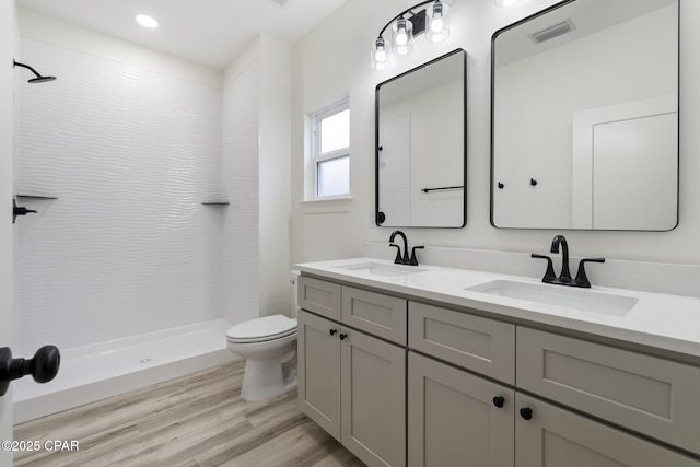 full bath with a sink, a tile shower, toilet, and wood finished floors