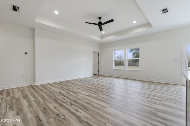 empty room with light wood-style floors, a tray ceiling, visible vents, and baseboards