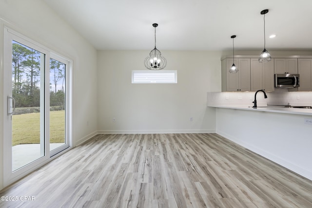 kitchen with hanging light fixtures, stainless steel microwave, light countertops, and backsplash