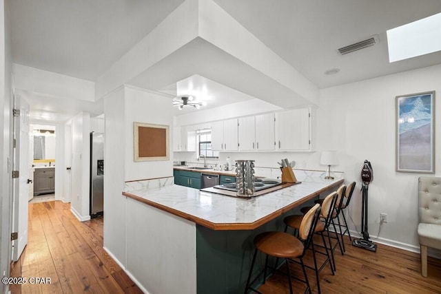 kitchen featuring visible vents, white cabinets, appliances with stainless steel finishes, a peninsula, and a kitchen bar