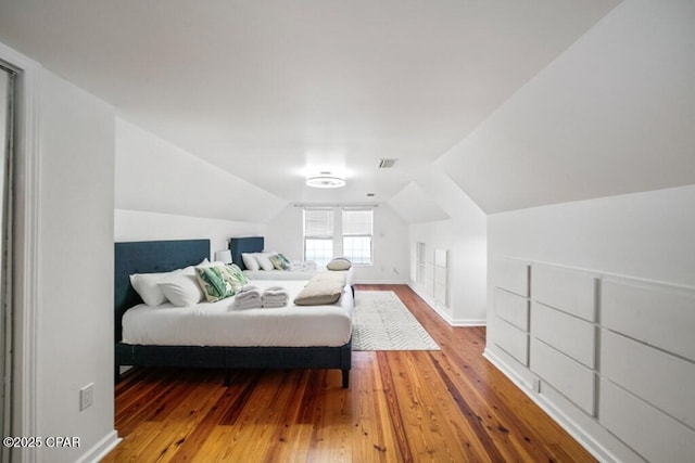 bedroom with lofted ceiling, baseboards, visible vents, and wood finished floors