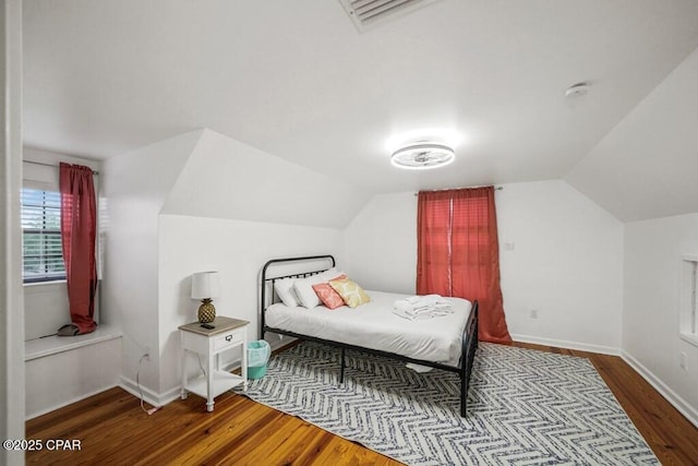 bedroom with lofted ceiling, wood finished floors, visible vents, and baseboards