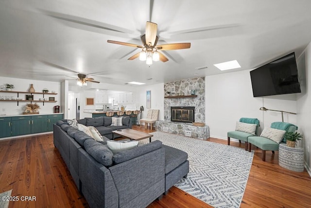 living area with ceiling fan, dark wood finished floors, and a stone fireplace